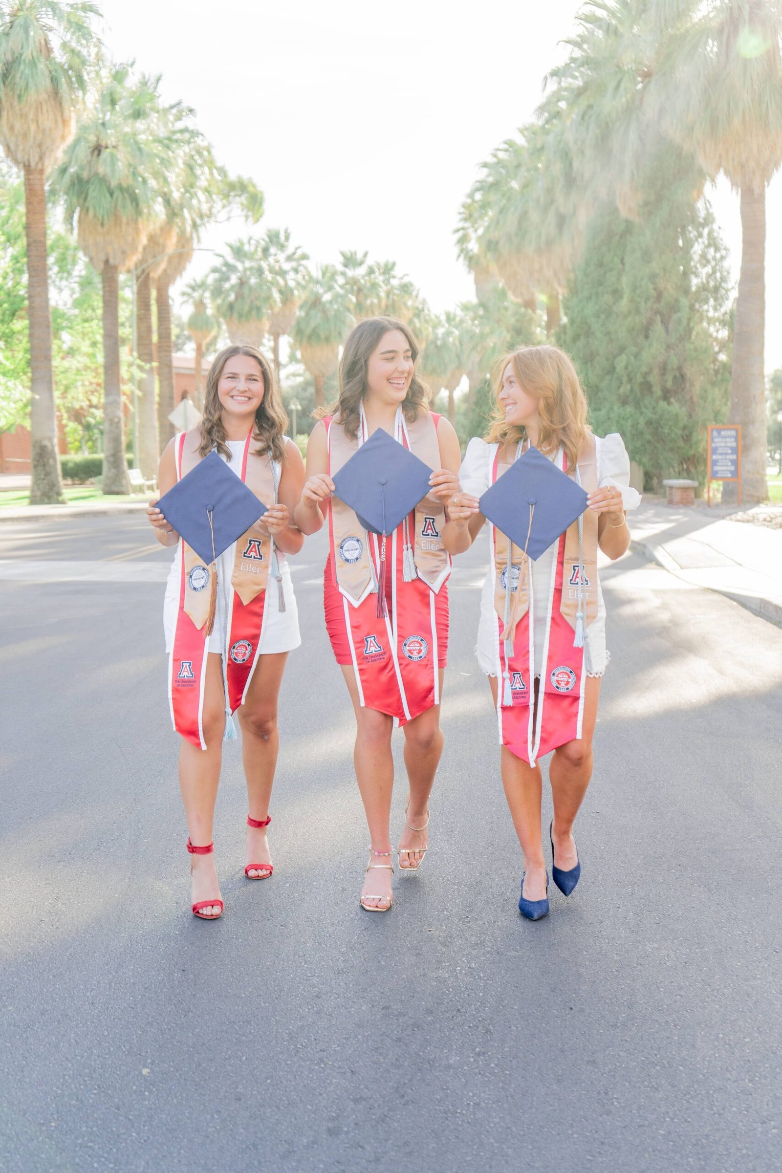 Three young women in graduation caps and gowns smiling together and celebrating.